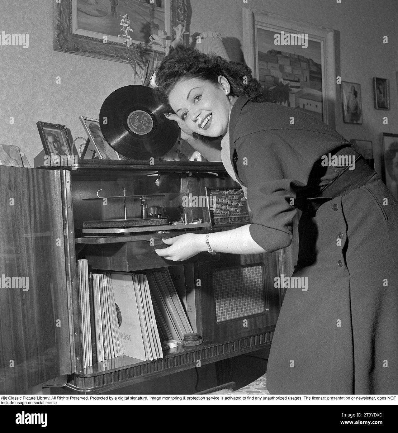 Frau am Gramophon in den 1950ern Schauspielerin Marion Sundh, 1927-1987 von dem Gramophon, einem Luxusmodell kombiniert mit einem Radio. Die Platten waren aus zerbrechlichem Material und die Geschwindigkeit der Aufnahme, wie sie sollte, betrug 78 Umdrehungen pro Minute. Schweden 1951. Conard Ref. 1689 Stockfoto