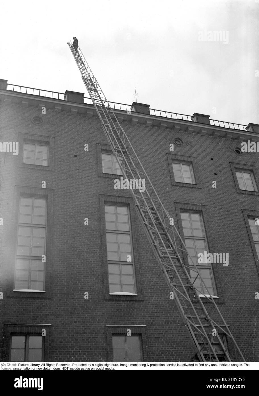 Feuer in den 1940ern Der Feuerwehrmann von Kungsholmen's Feuerwache geht die Leiter hoch, die gegen ein Haus aufgestellt ist. Schweden Februar. 1940. Kristoffersson Ref. 56-10 Stockfoto