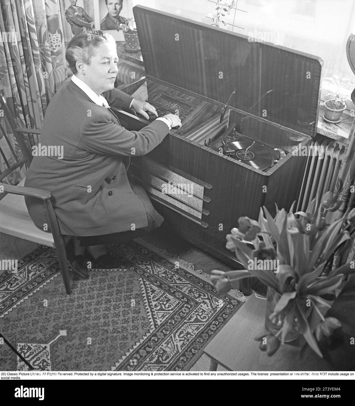 Frau am Gramophon in den 1940ern Kai Gullmar. Musikkomponist und Sänger, die ein Lied hören, das auf dem Grammophon gespielt wird. Bei diesem Modell gab es Möglichkeiten, den Klang zu ändern, um das Hörerlebnis zu verbessern. Die Platten waren aus zerbrechlichem Material und die Geschwindigkeit der Aufnahme, wie sie sollte, betrug 78 Umdrehungen pro Minute. Schweden 1943. Kristoffersson Ref. C9-1 Stockfoto