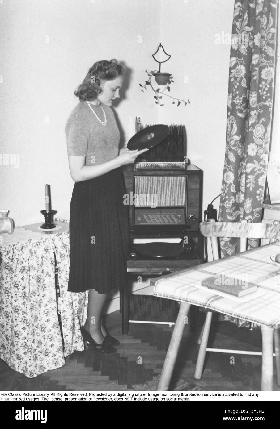 Frau am Gramophon in den 1940ern Die Schauspielerin Gunn Wållgren, 1913–1983, besitzt eine der Aufzeichnungen, um das Label zu lesen, das Informationen über das aufgenommene, den Namen der Lieder und den Künstler enthielt. Im Allgemeinen war das Logo der Plattenfirma auf dem Etikett zu sehen. Die Platten waren aus zerbrechlichem Material und die Geschwindigkeit der Aufnahme, wie sie sollte, betrug 78 Umdrehungen pro Minute. Ein Funkgerät sitzt auf dem Grammophon. Schweden 1947 Stockfoto