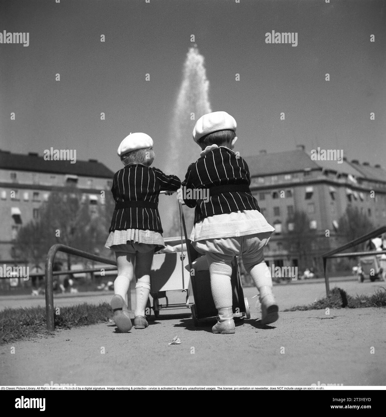 Für einen Spaziergang in den 1940ern Zwei kleine Kinder spielen im Park und schieben Puppenwagen. Sie tragen fast die gleiche Kleidung, schwarze Jacken mit weißen Streifen und eine weiße Baskenmütze. Schweden Mai 1940 Kristoffersson Ref. 133-12 Stockfoto