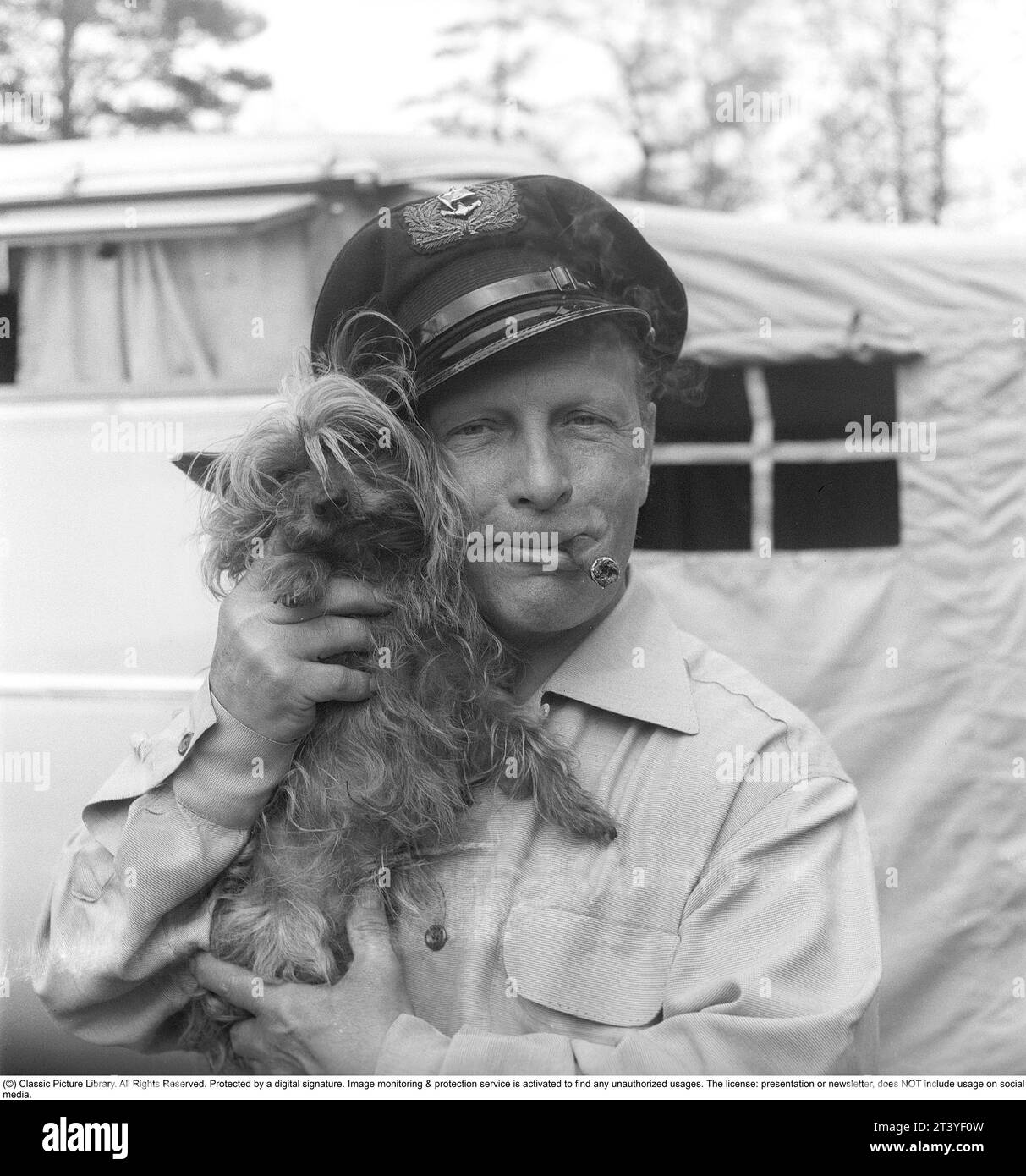In den 1950er Jahren Ein Mann, der zusammen mit seinem kleinen Hund dargestellt wird, den er sichtbar mag und hält. Er raucht eine Zigarre und trägt eine Mütze. Schweden 1951. Kristoffersson Ref. BP30-6 Stockfoto