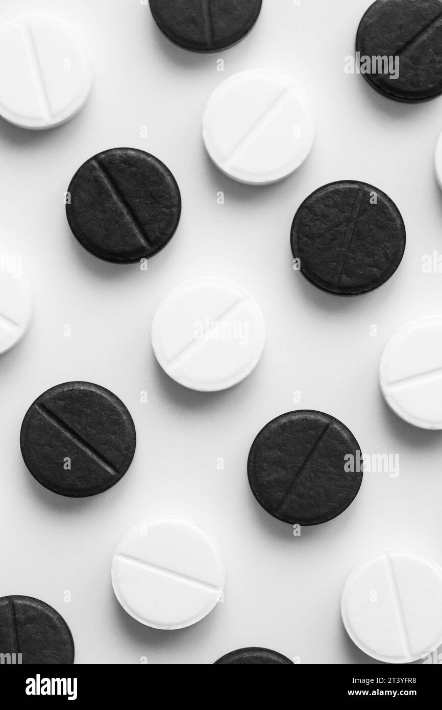 Vertikale Nahaufnahme der Draufsicht von schwarz-weißen Pillen liegen genau in einer Reihe auf einem weißen Tisch. Isolierter pharmazeutischer minimalistischer Hintergrund Stockfoto