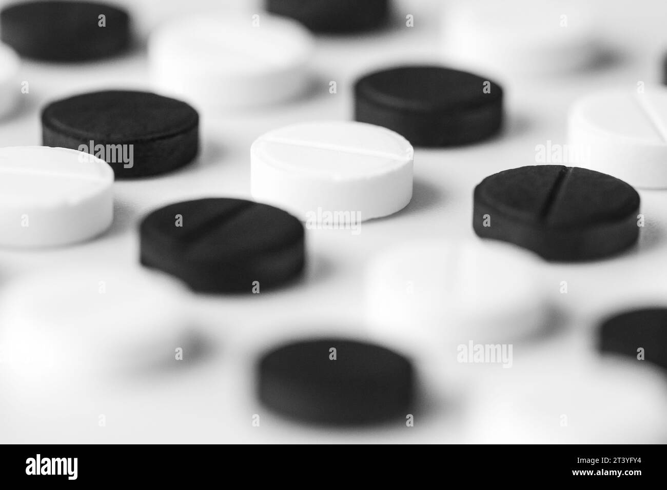 Nahaufnahme von schwarz-weißen Pillen liegen genau in einer Reihe auf einem weißen Tisch. Isolierter pharmazeutischer Hintergrund Stockfoto