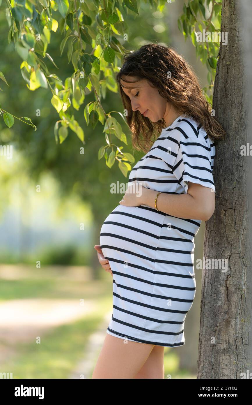Junge schwangere Frau im Park mit einem schwarz-weißen Kurzkleid Stockfoto