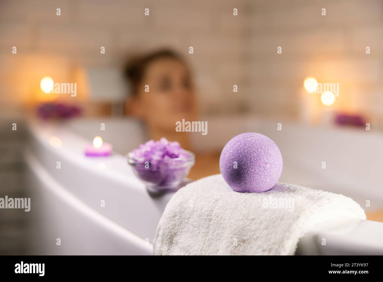 Heim-Spa. Frau, die sich in der Badewanne im Kerzenlicht entspannt und Badbombe und Meersalzkristalle für die Körperhaut mit Feuchtigkeit versorgt Stockfoto