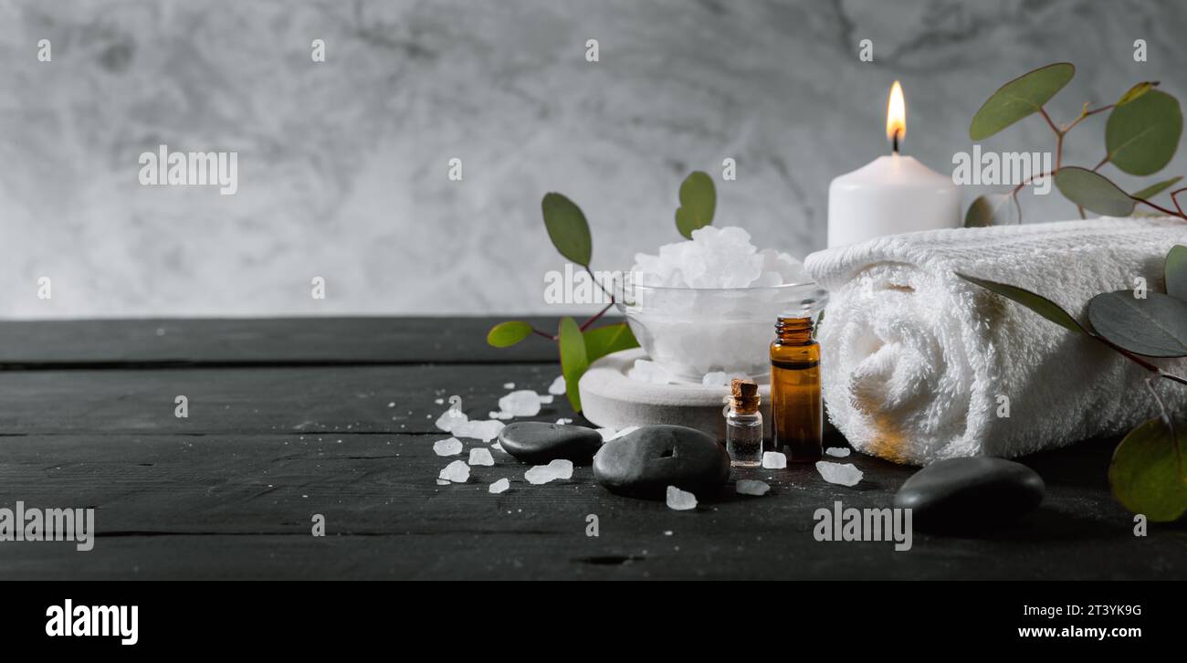 Wellness-Spa-Behandlung. Körperpflegeartikel auf schwarzem Holztisch mit Marmorhintergrund. Ätherische Öle, Handtuch, Badkristalle und Kerze Stockfoto