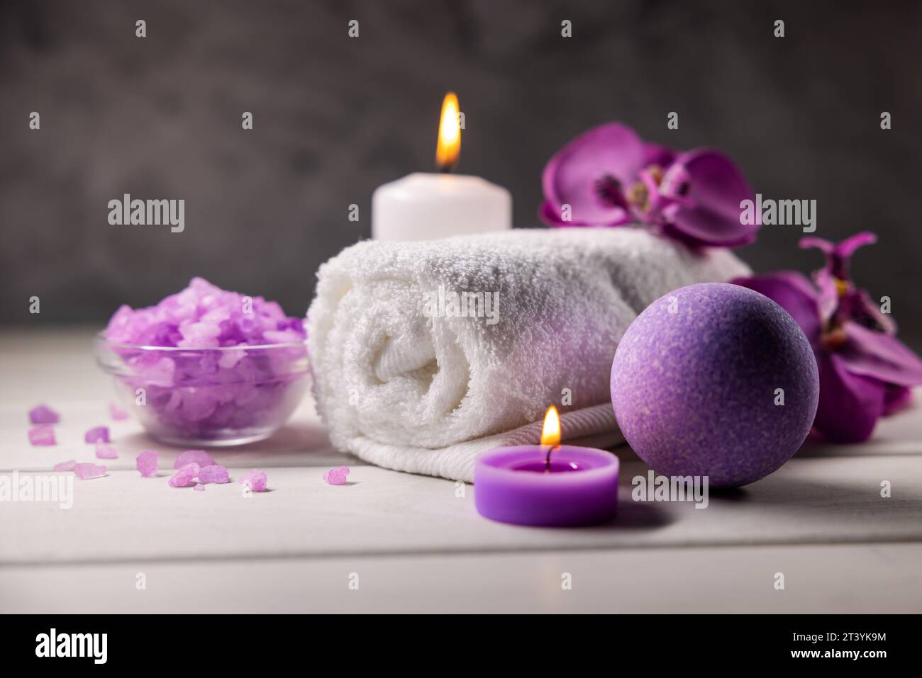 Lila Badebombe, Meersalzkristalle, Handtuch und Duftkerzen auf Holztisch. Körperhautpflege. Wellness-Spa Stockfoto