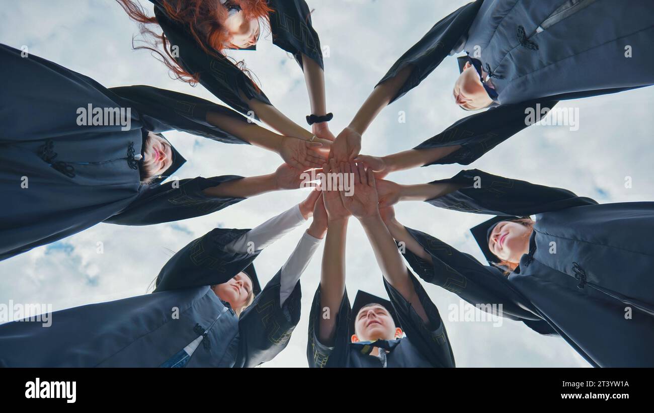 Team von College- oder Universitätsstudenten, die den Abschluss feiern. Gruppe glücklicher erfolgreicher Absolventen in akademischen Hüten und Gewändern, die im Kreis stehen und Stockfoto