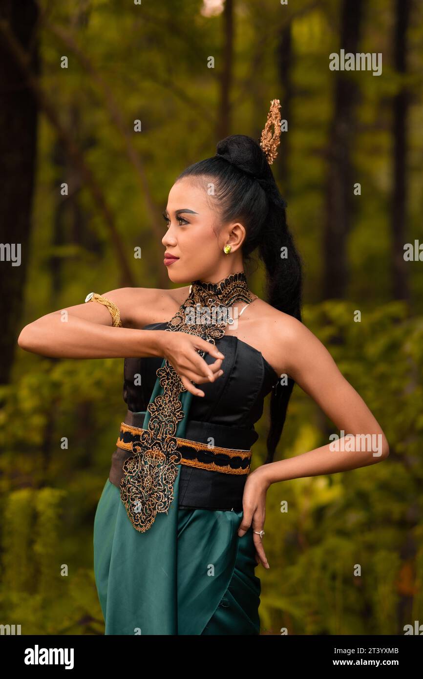 Wunderschöne indonesische Tänzer mit traditionellen grünen Kostümen und schwarzen Haaren, die nach der Aufführung im Wald posieren Stockfoto