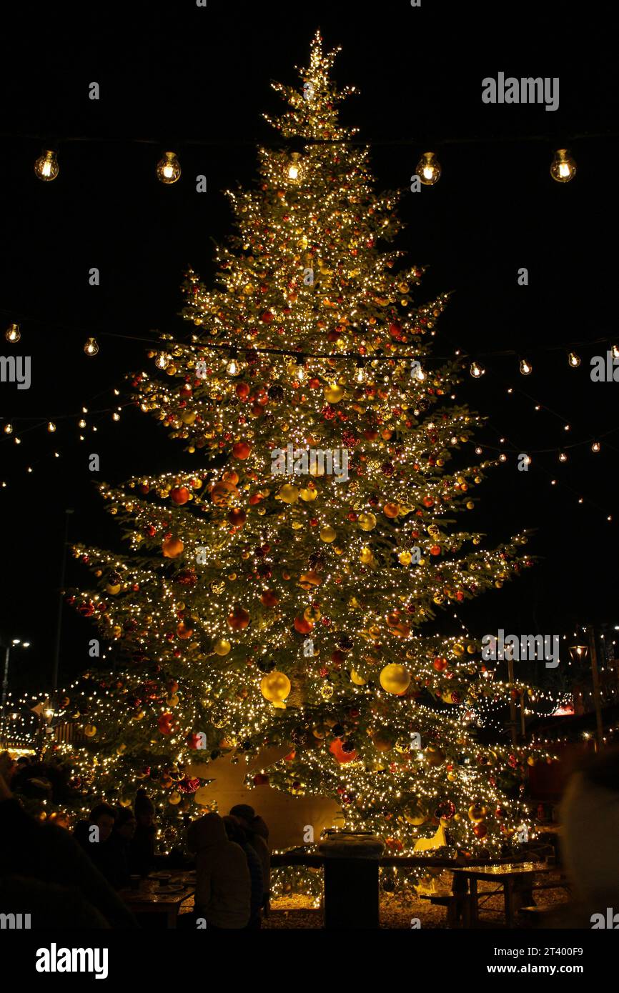 Nächtlicher Weihnachtsmarkt in der Schweiz. Wunderschön beleuchteter, wunderschöner Weihnachtsbaum mit goldenen Lichtern, goldenen und roten Kugeln draußen auf Schwarz Stockfoto