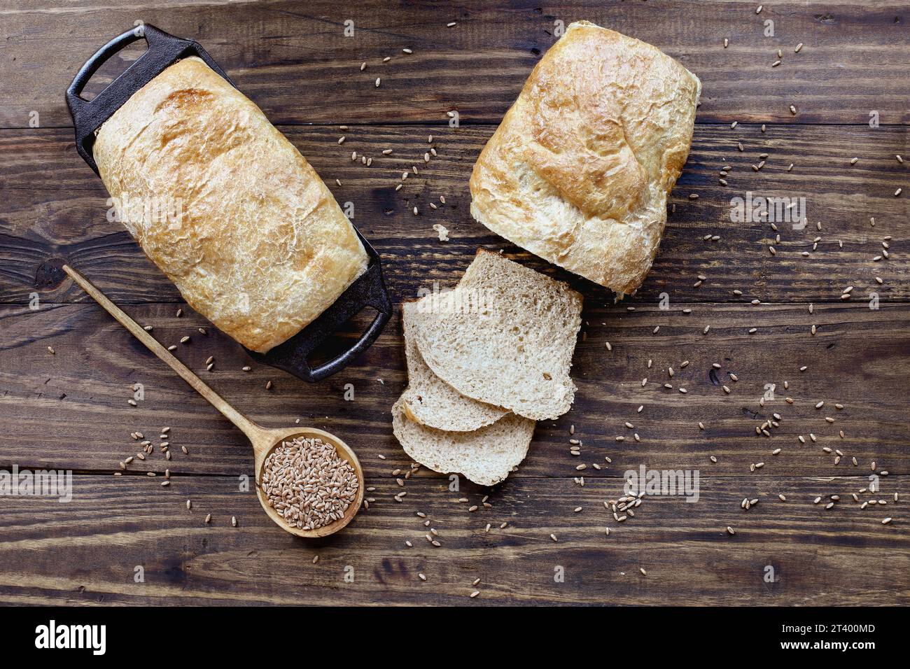Über dem Tisch sehen Sie frisch gebackene Vollkornbrotlaibe mit Holzlöffel gefüllt mit Getreide. Gemeinkosten. Stockfoto