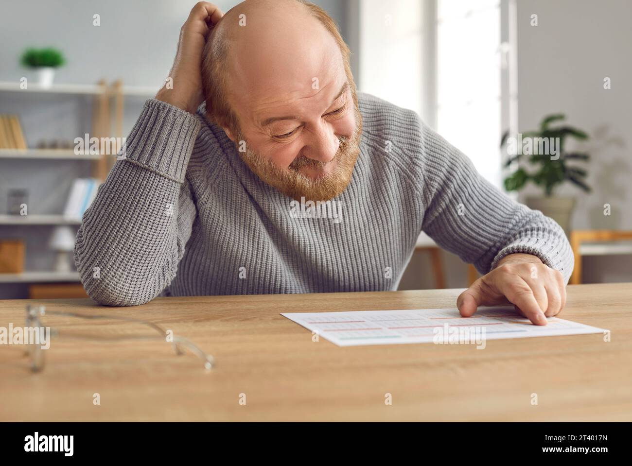 Ein älterer Mann mit Alzheimer-Krankheit wird verwirrt, wenn er sich den Kalender auf dem Tisch ansieht Stockfoto