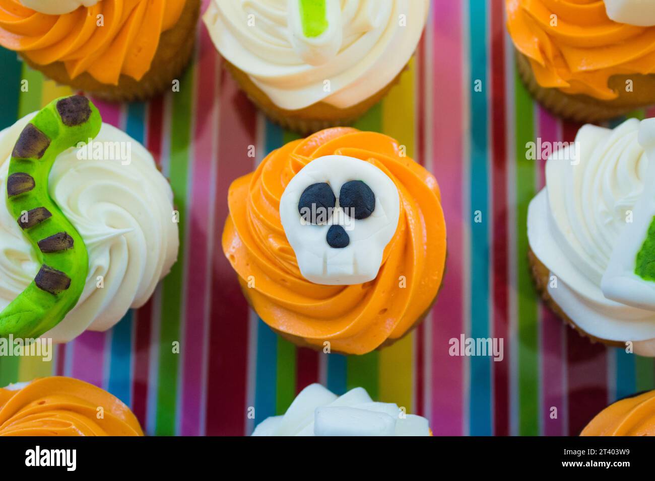 Dekorierte Cupcakes im Halloween-Thema. Orangenfrost mit einer Totenkopfdekoration oben. Stockfoto