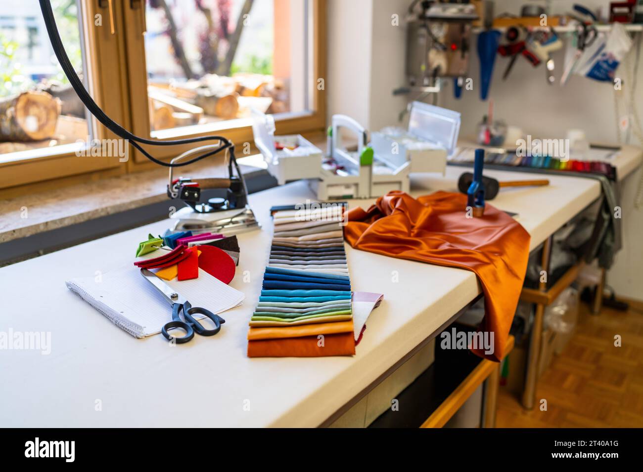 In der Näh- oder Schneiderwerkstatt wird ein Tisch mit Nähutensilien präsentiert: Stoffmuster, Scheren, Bügeleisen, Farbpalette, Seidenstoffe und Werkzeuge, Stockfoto