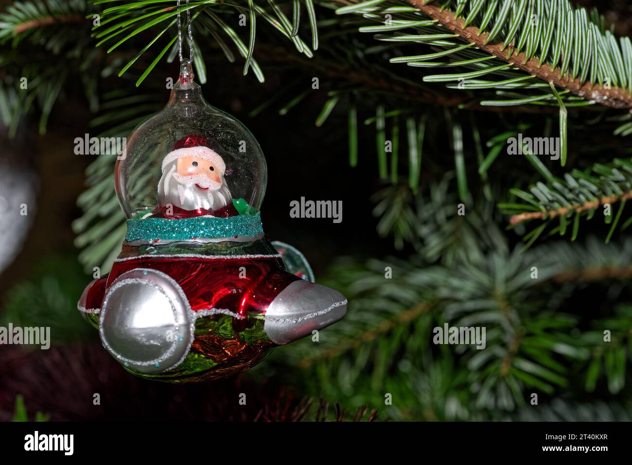 Nahaufnahme eines roten Raumschiffs mit dem Weihnachtsmann, der an Cristmas-Baum hängt, gegen grüne Äste Stockfoto