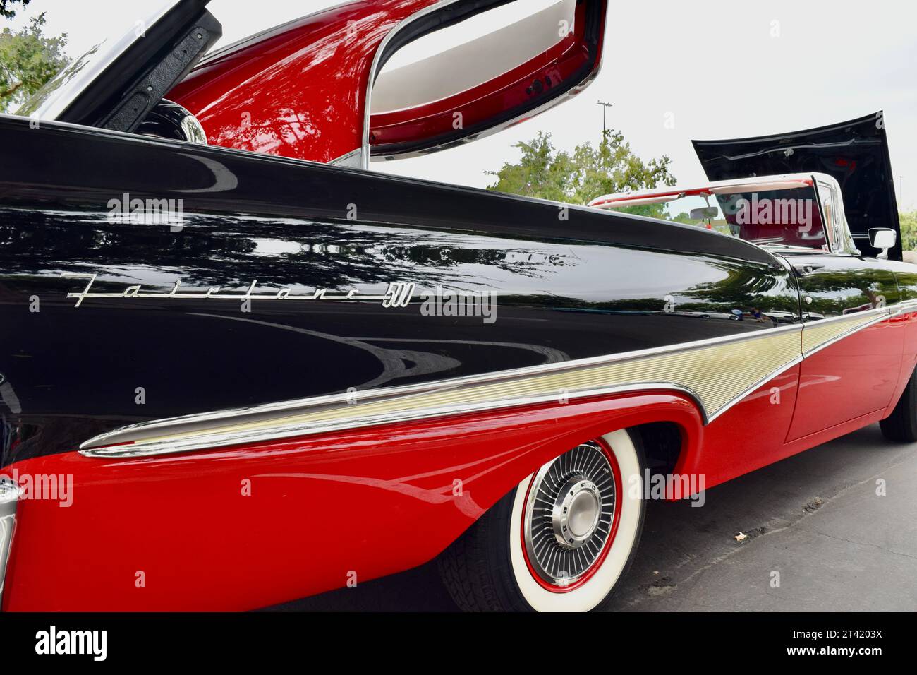 Ein schwarz-roter zweitüriger Sportwagen mit Motorhaube, der auf einem Parkplatz mit Bäumen im Hintergrund auf einer Oldtimer-Show geparkt wird Stockfoto