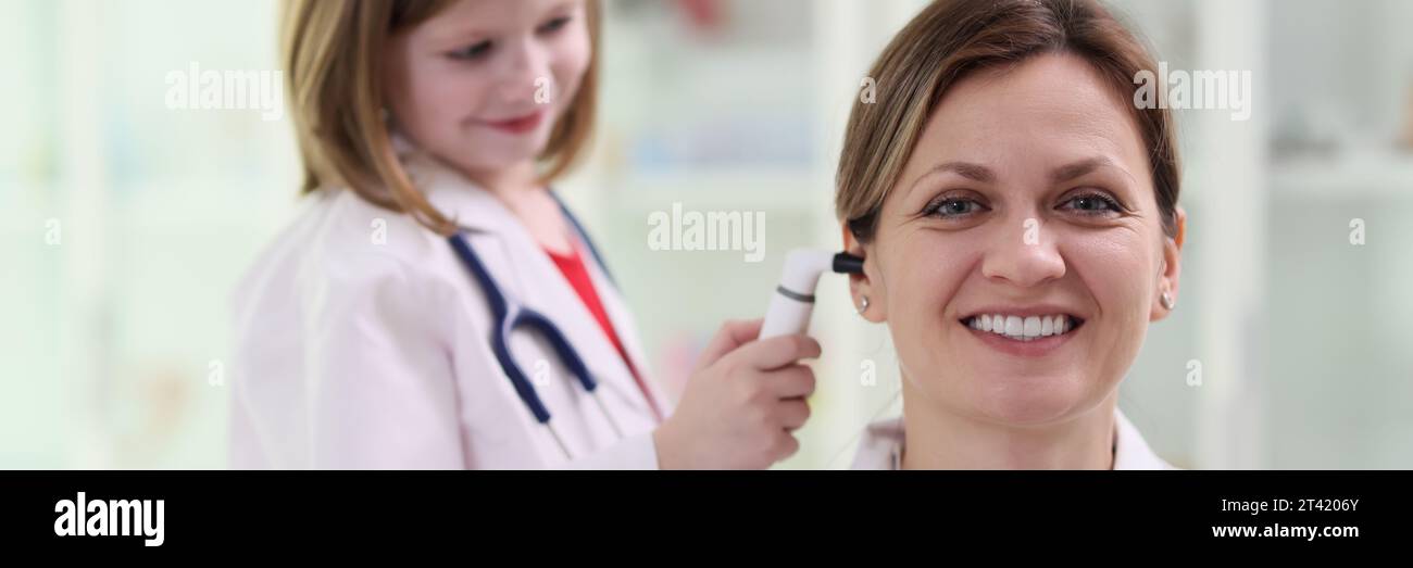 Süßes kleines Mädchen in medizinischer Uniform überprüft Ohr der Frau Stockfoto