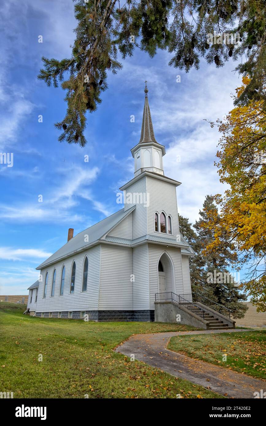 Ein Bürgersteig führt zu einer kleinen Landkirche unter blauem Himmel im Herbst in der Nähe von Moskau, Idaho. Stockfoto