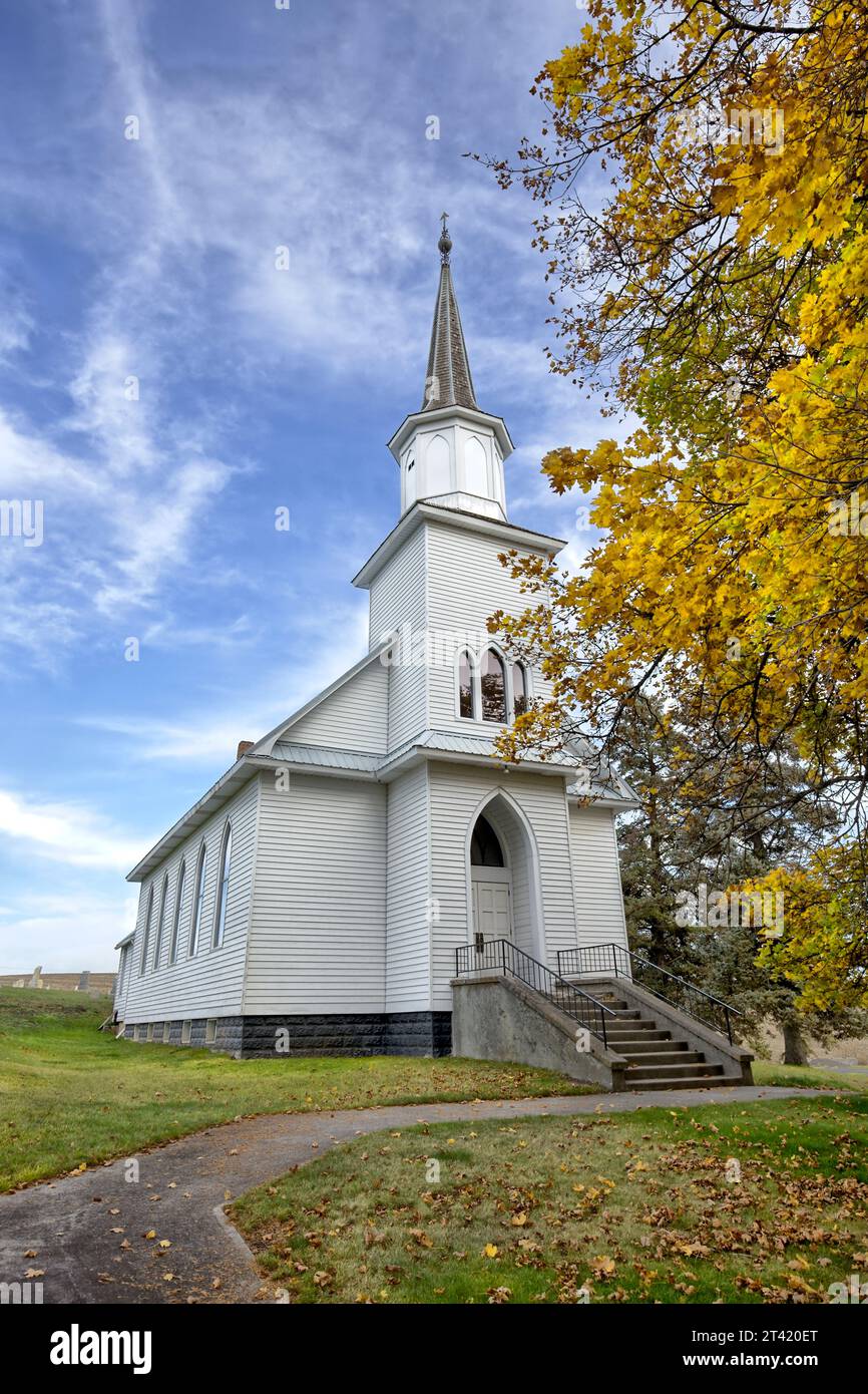 Ein Bürgersteig führt zu einer kleinen Landkirche unter blauem Himmel im Herbst in der Nähe von Moskau, Idaho. Stockfoto