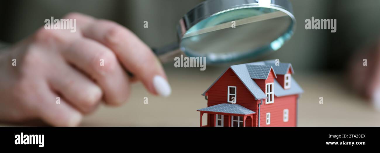 Eine Frau hält eine Lupe über ein kleines Stadthausmodell Stockfoto