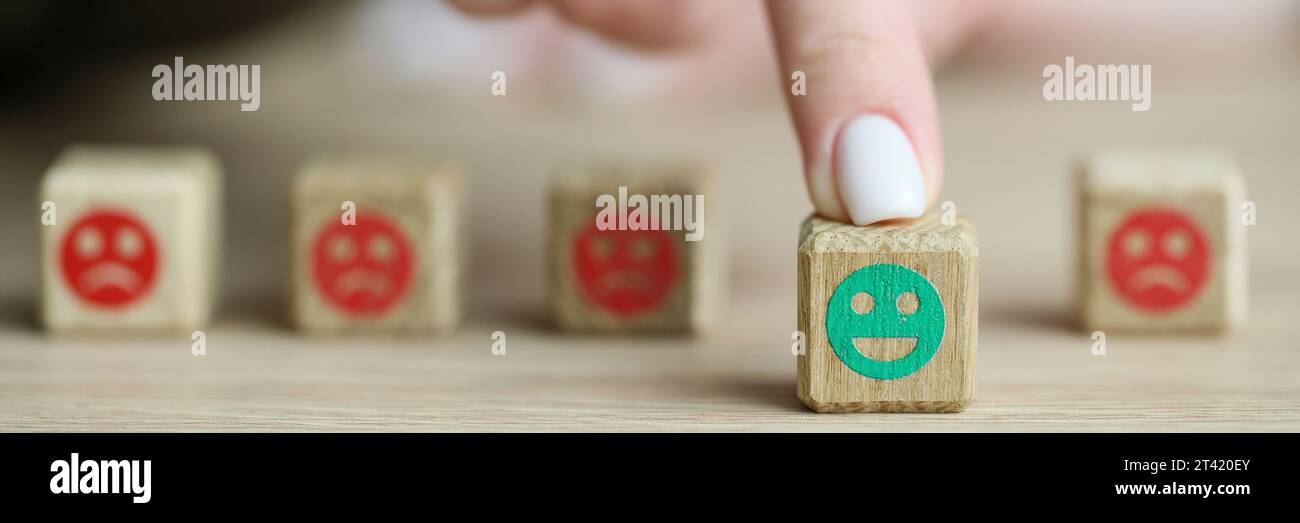 Der Finger einer Frau bewegt einen hölzernen Würfel mit positiven Emoji-Bewegungen Stockfoto