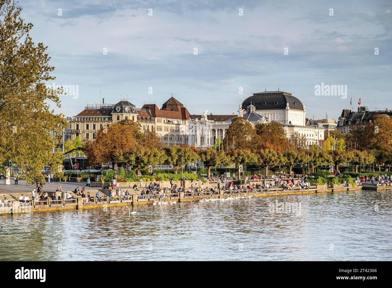 Menschen, die an einem Kai am Ufer des Zürichsees sitzen, Opernhaus im Hintergrund, Zürich, Kanton Zürich, Schweiz Stockfoto
