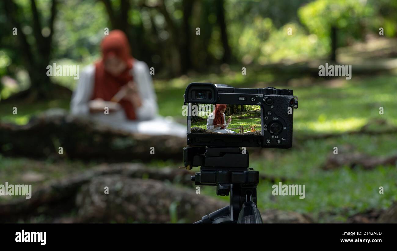 Muslimische Frau im Hijab sitzt im Park und macht ein Bastelvideo. Stockfoto