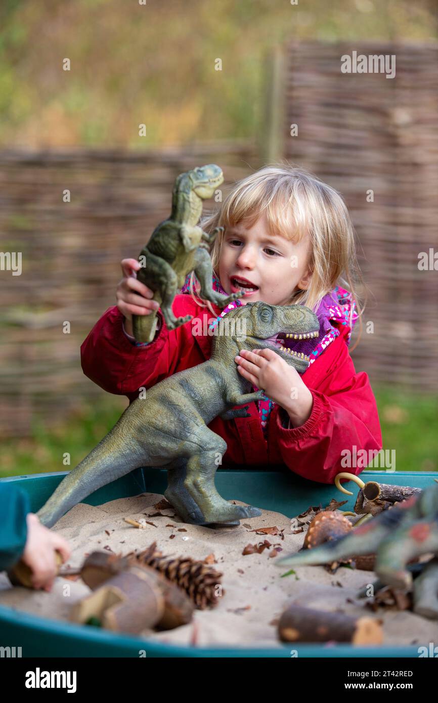 Ein Mädchen in einer britischen Kinderschule, das draußen mit Spielzeugdinosauriern in einem Sandtablett spielt Stockfoto