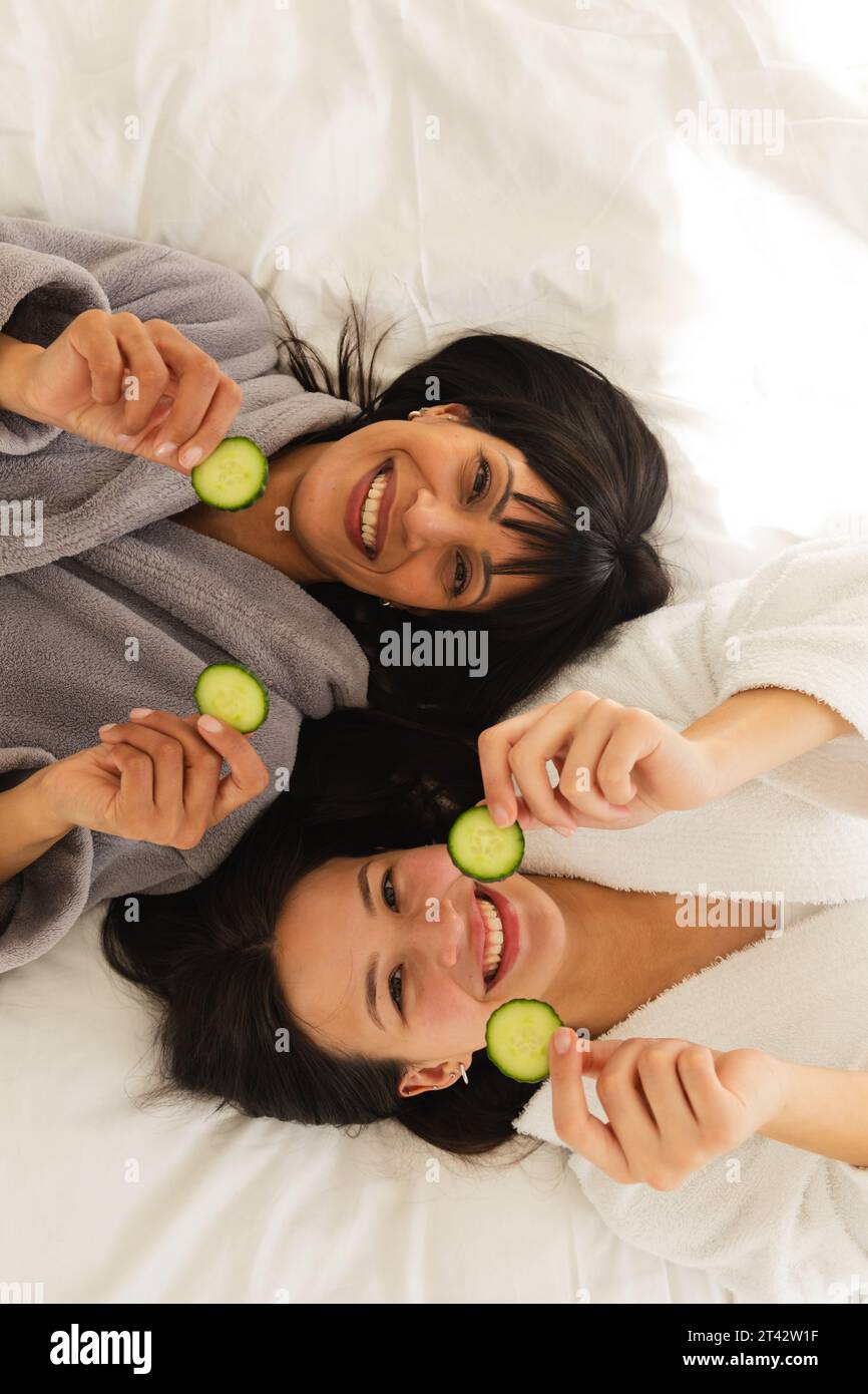 Diverse Mutter und Tochter in Bademänteln, liegend auf Bett mit Gurkenscheiben zu Hause, Kopierraum Stockfoto