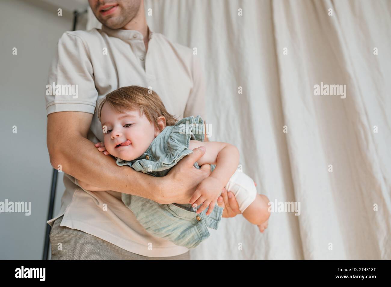 Vater, der in einem Wohnzimmer steht und seine Tochter in den Armen schaukelte Stockfoto