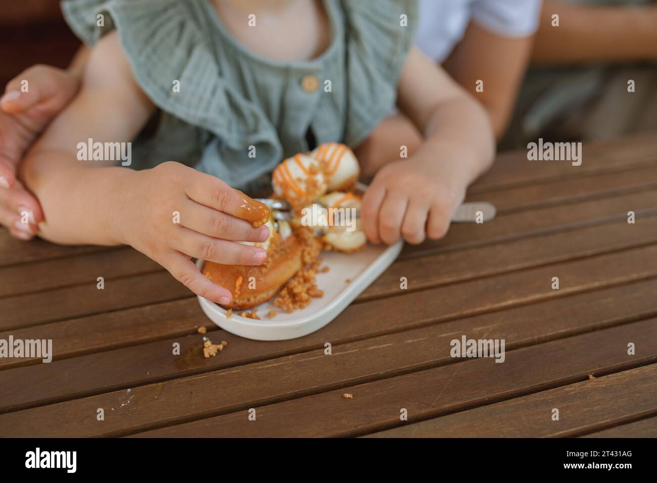 Nahaufnahme eines Mädchens, das auf dem Schoß ihrer Mutter sitzt und mit ihren Fingern ein Dessert isst Stockfoto