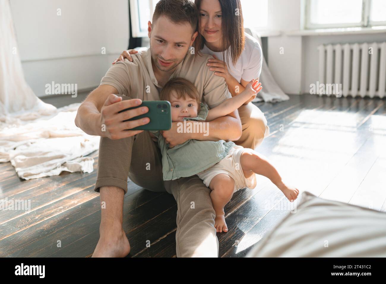 Junge Paare, die auf dem Boden sitzen und ein Selfie im Wohnzimmer mit ihrer Tochter machen Stockfoto