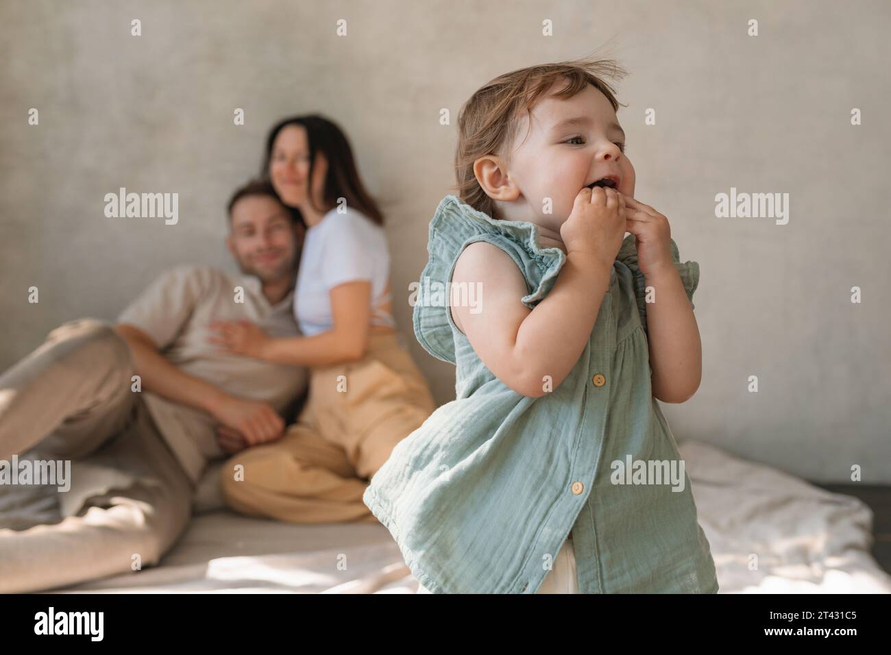 Glückliche Eltern sitzen auf dem Boden in einem Wohnzimmer und beobachten ihre Tochter beim Spielen Stockfoto