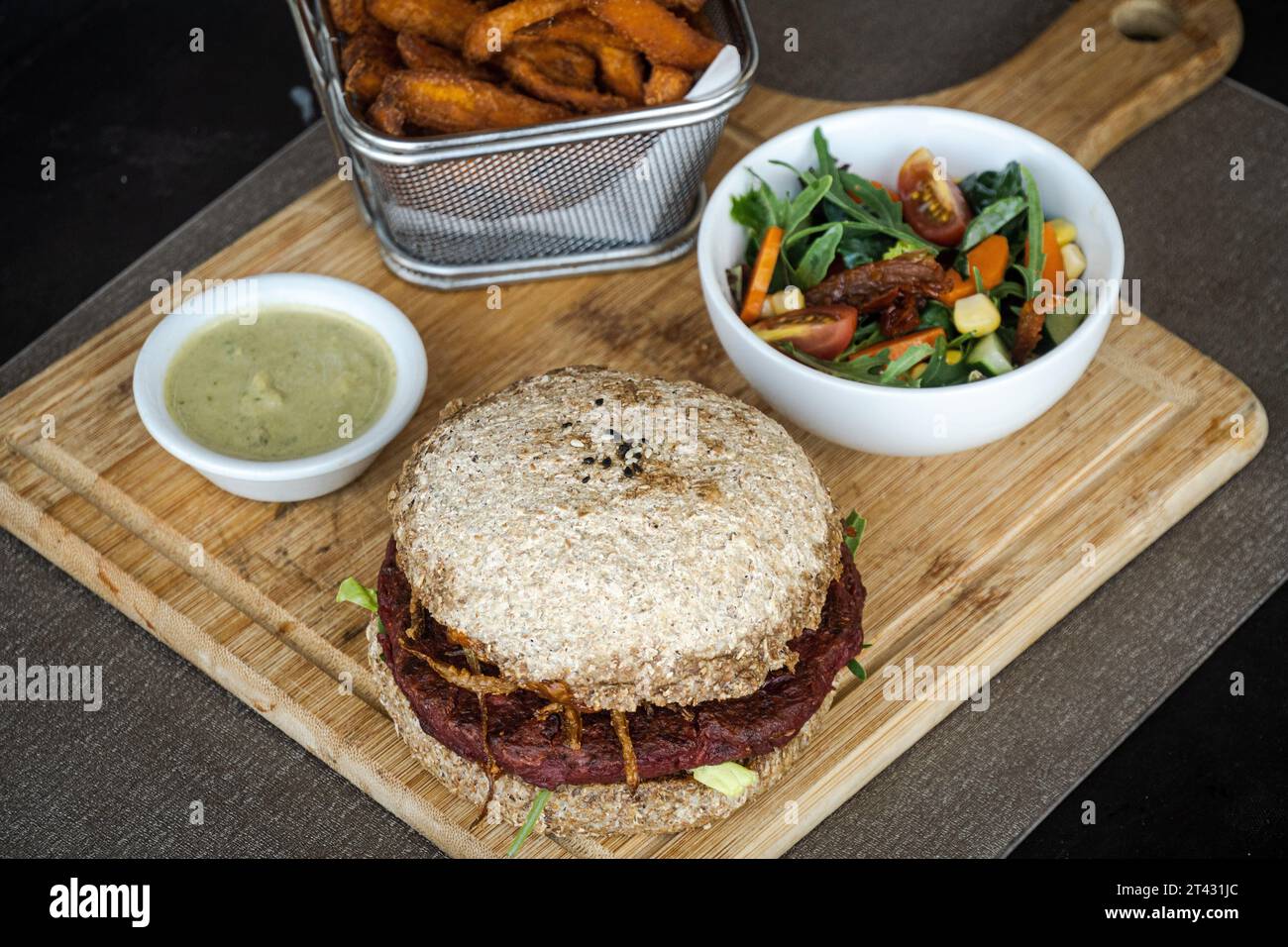Nahaufnahme eines Rote-Bete-Bohnen-Burgers mit Süßkartoffelfritten, Salat und Dippsoße Stockfoto