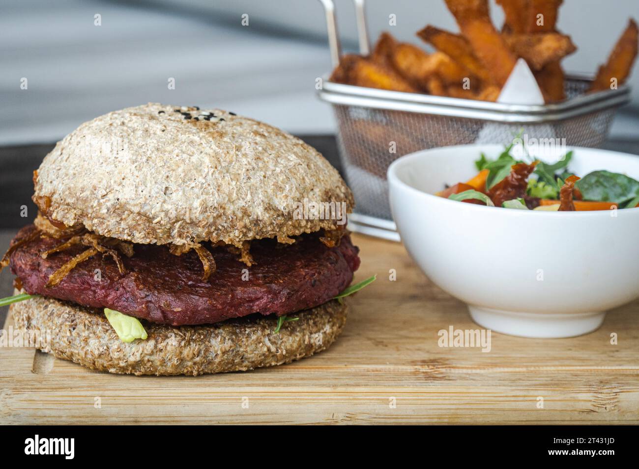 Nahaufnahme eines Rote-Bete-Bohnen-Burgers mit gebratenen Zwiebeln, Süßkartoffelfritten, Salat und Dippsoße Stockfoto