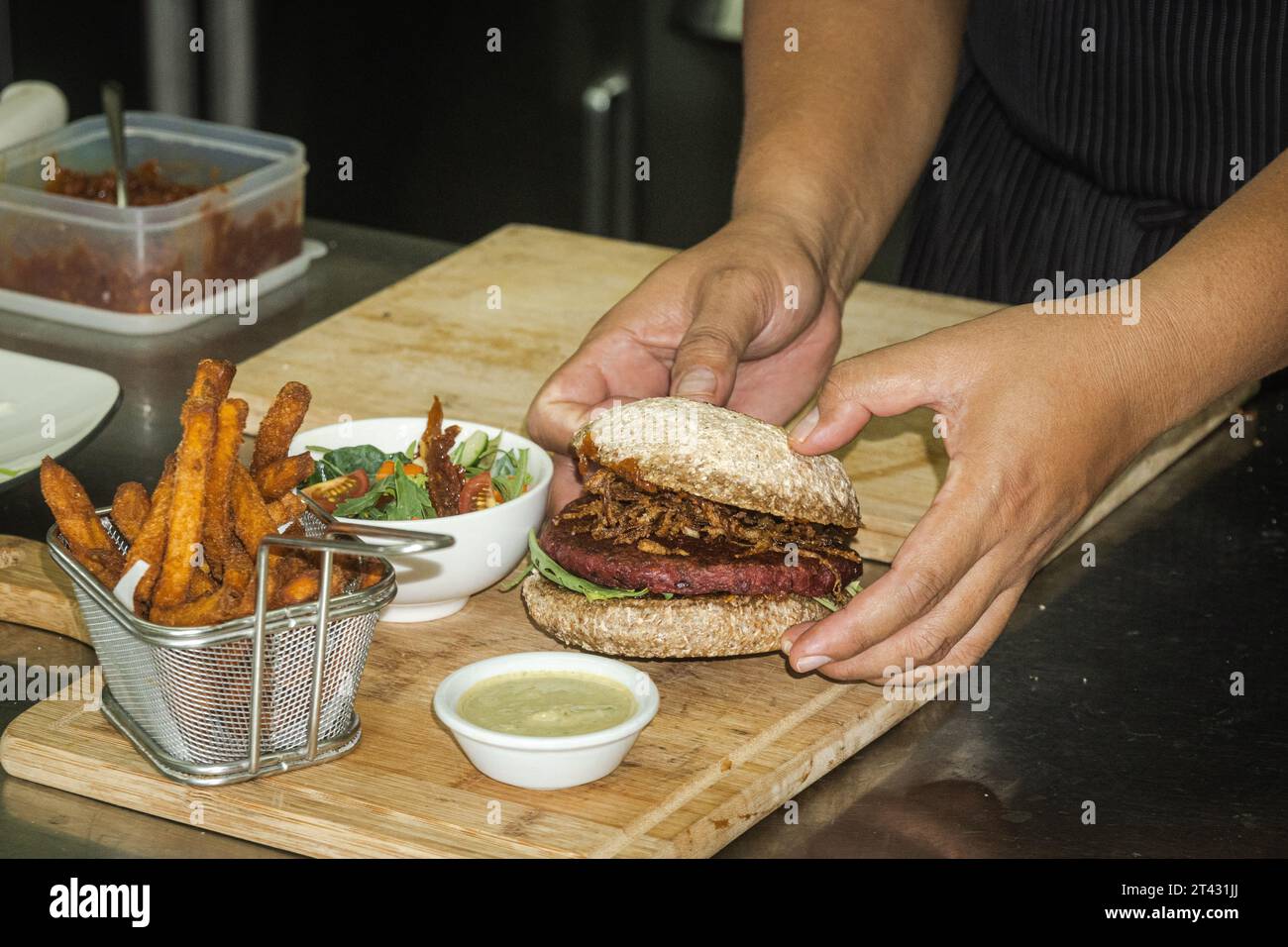 Nahaufnahme eines Küchenchefs, der einen Rote-Bete-Bohnen-Burger mit Süßkartoffelfritten, Salat und Dippsoße zubereitet Stockfoto