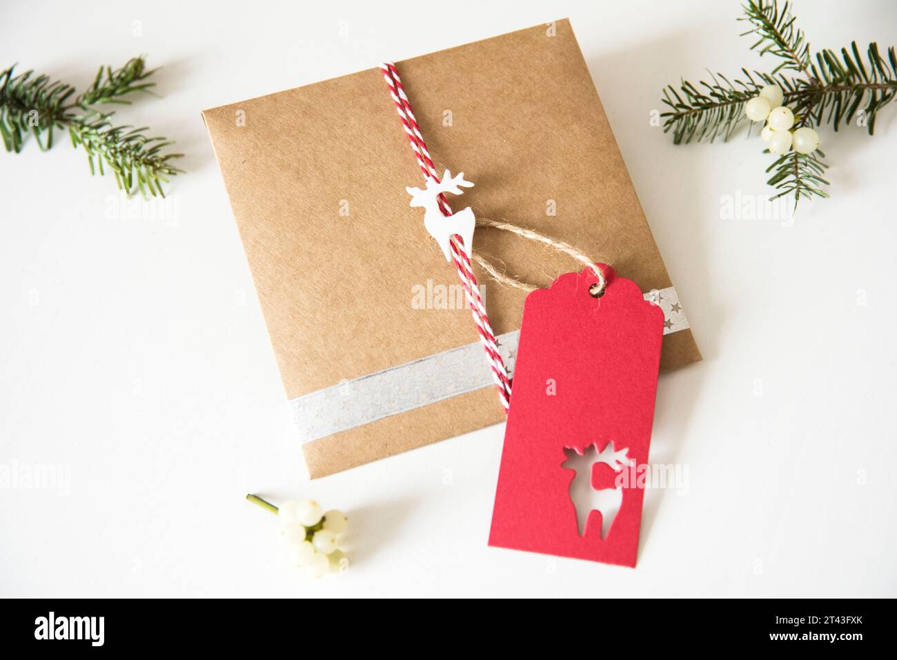 Rustikale Geschenkverpackung mit Bastelpapier, verziert mit einem charmanten Rentier und duftenden Tannenzweigen, die die Essenz der weihnachtlichen Tradition einfangen Stockfoto