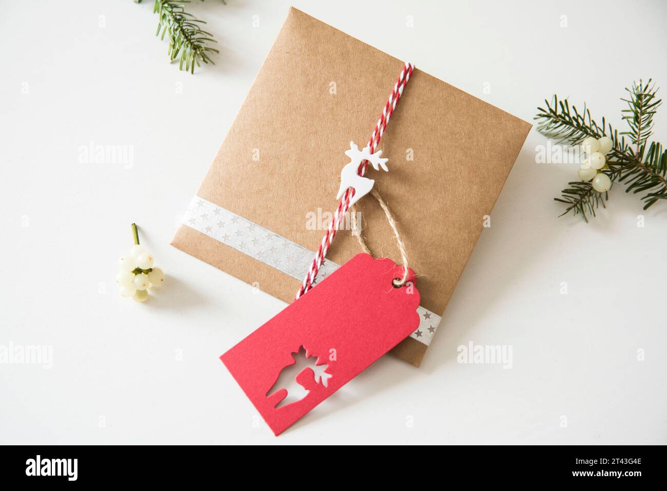Rustikale Geschenkverpackung mit Bastelpapier, verziert mit einem charmanten Rentier und duftenden Tannenzweigen, die die Essenz der weihnachtlichen Tradition einfangen Stockfoto