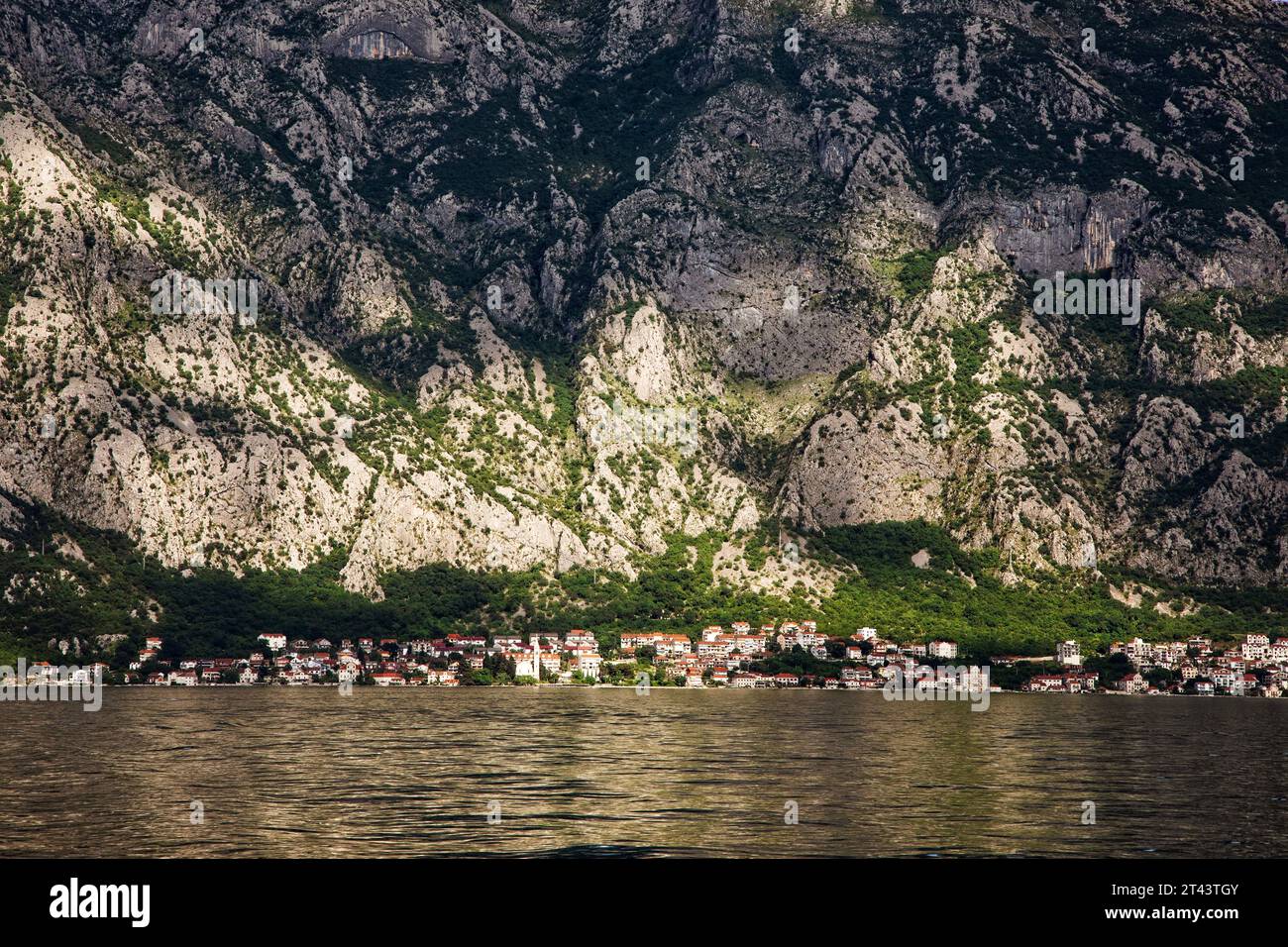 Kleinstädte liegen unter senkrechten Felswänden und umarmen die Küste in der Bucht von Kotor entlang der Adriaküste Montenegros. Stockfoto