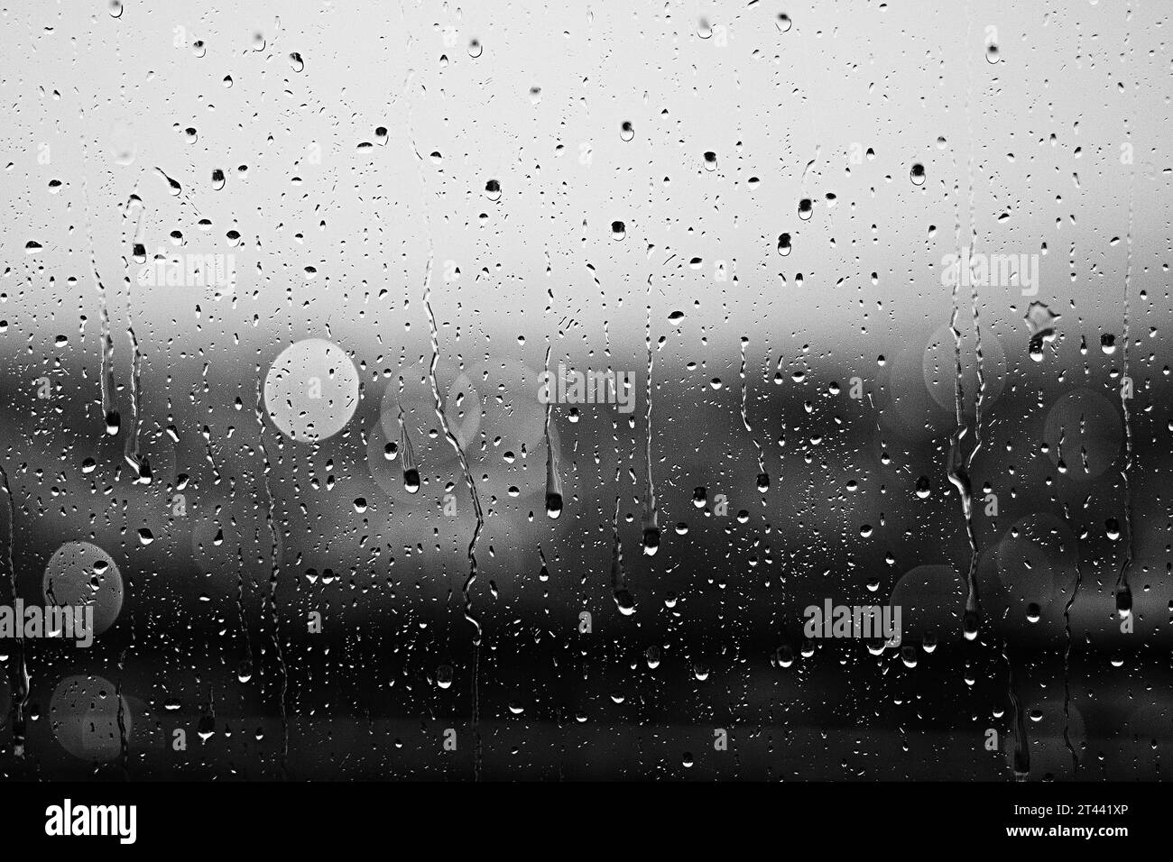 Regentropfen fließen durch das Fenster. Nahaufnahme eines Schwarzweißfotos von Regentropfen auf dem Glasfenster Stockfoto