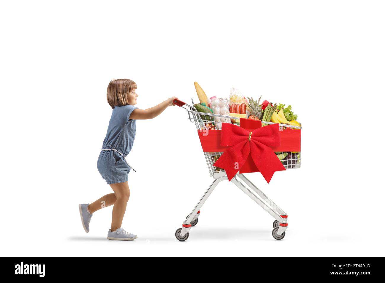 Profilaufnahme eines kleinen Mädchens, das einen Einkaufswagen schiebt, gebunden mit rotem Band, isoliert auf weißem Hintergrund Stockfoto