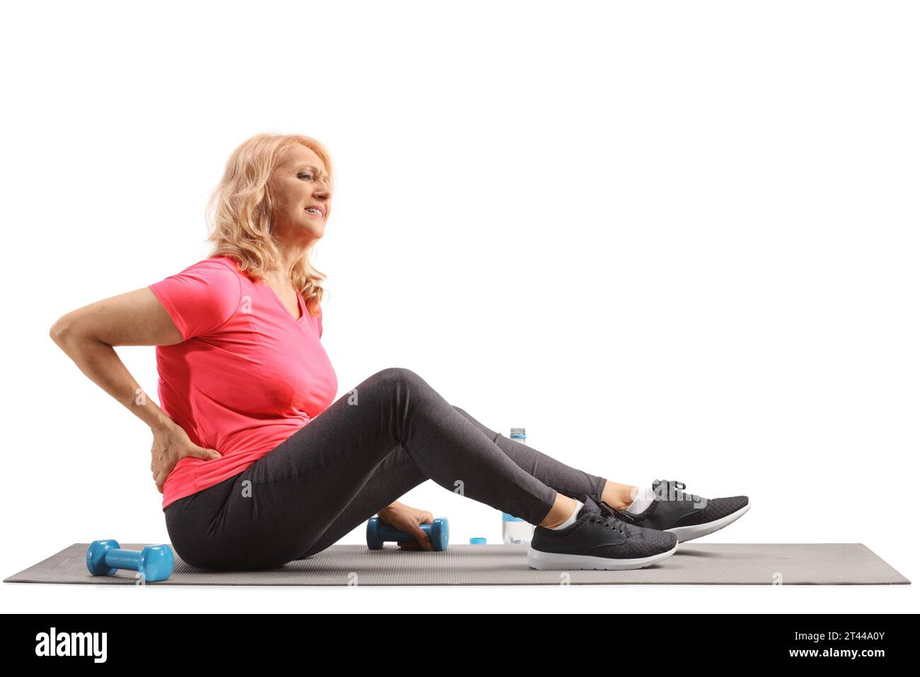 Reife Frau in Sportbekleidung, die auf einer Trainingsmatte sitzt und ihre schmerzhafte Wirbelsäule isoliert auf weißem Hintergrund hält Stockfoto