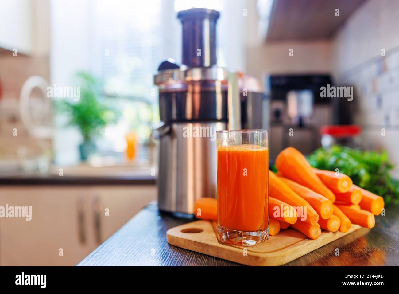 Ein Glas frisch gepressten Karottensaft, Karotten und Saftpresse in der Küche Stockfoto