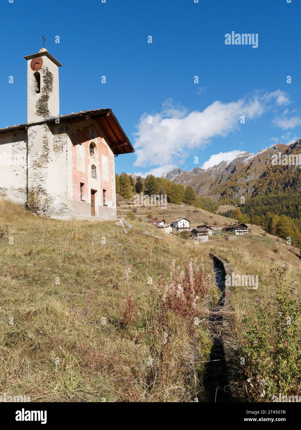 Malerische abgelegene Kirche mit Glockenturm und Dorf dahinter in abgelegener ländlicher Umgebung an einem Herbsttag im Aostatal NW Italien. Oktober 2023 Stockfoto