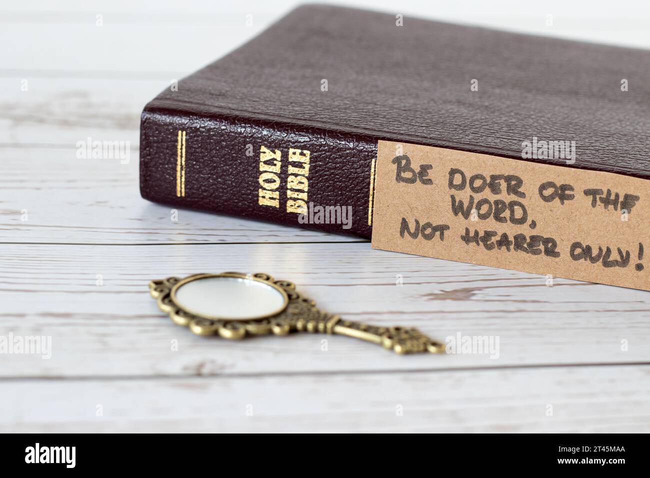 Sei Täter des Wortes, nicht nur Hörer, handgeschriebener Vers mit geschlossenem heiligem Bibelbuch und antikem goldenem Spiegel auf Holz. Eine Nahaufnahme. Jakobus 1:22 Schrift Stockfoto