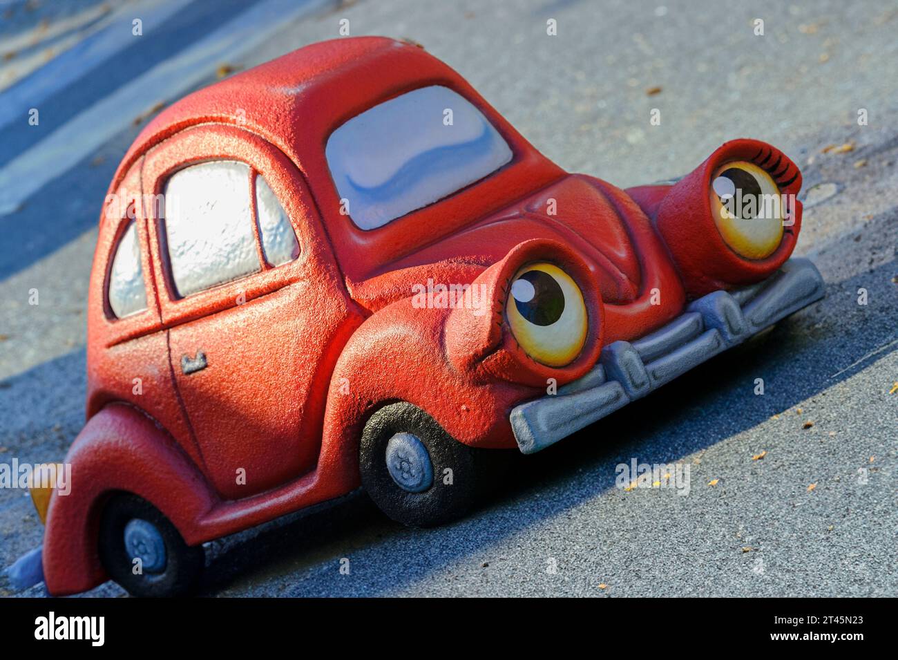 Anthropomorphes rotes Spielzeugauto, das auf einer Asphaltstraße aufwärts fährt Stockfoto