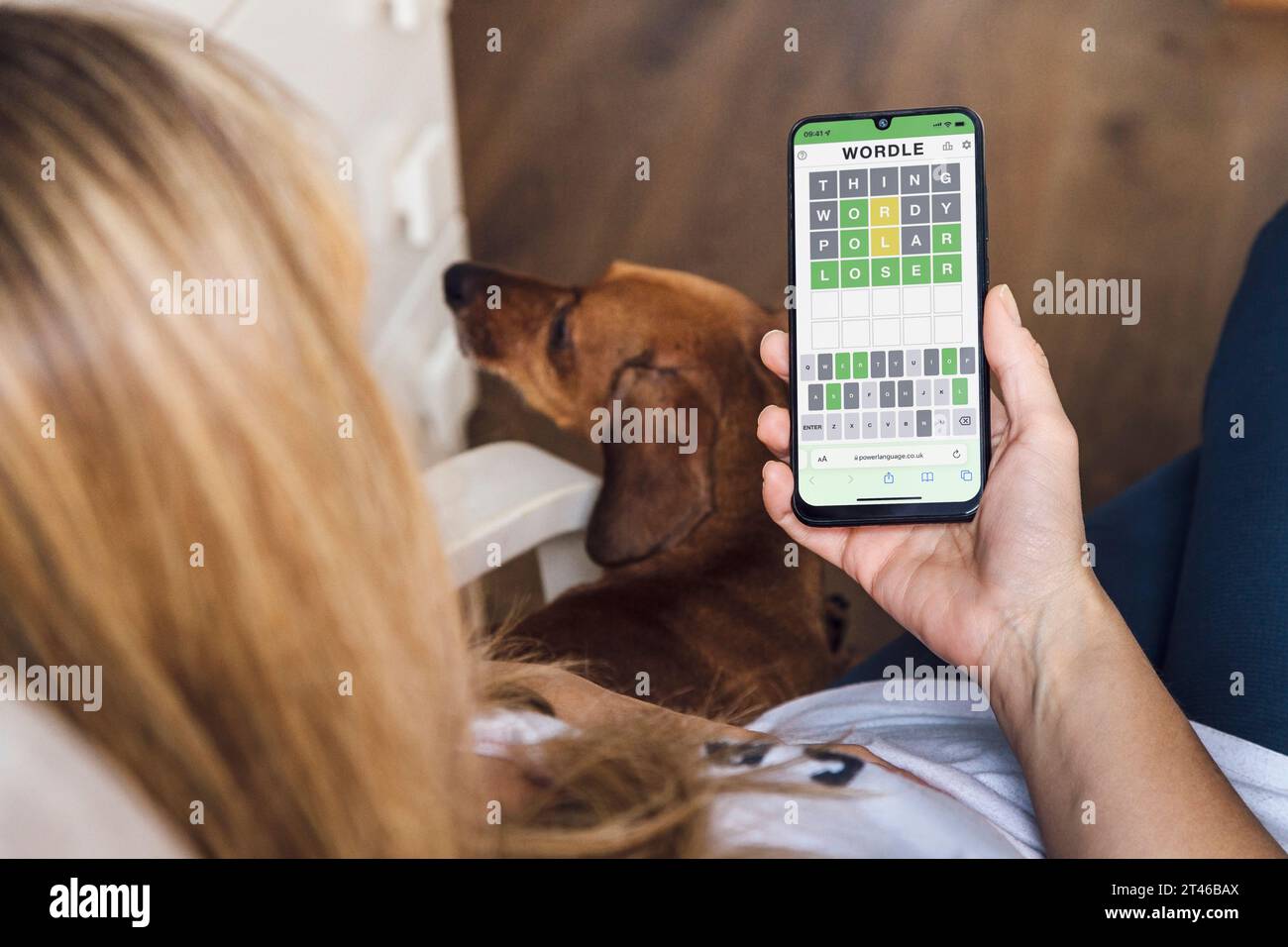 Die Frau ist bequem zu Hause und spielt Wordle auf ihrem Handy. Beliebtes Wortspiel, das auf einem Smartphone-Bildschirm angezeigt wird. Rosario, Argentinien - 27. Oktober 2023. Stockfoto