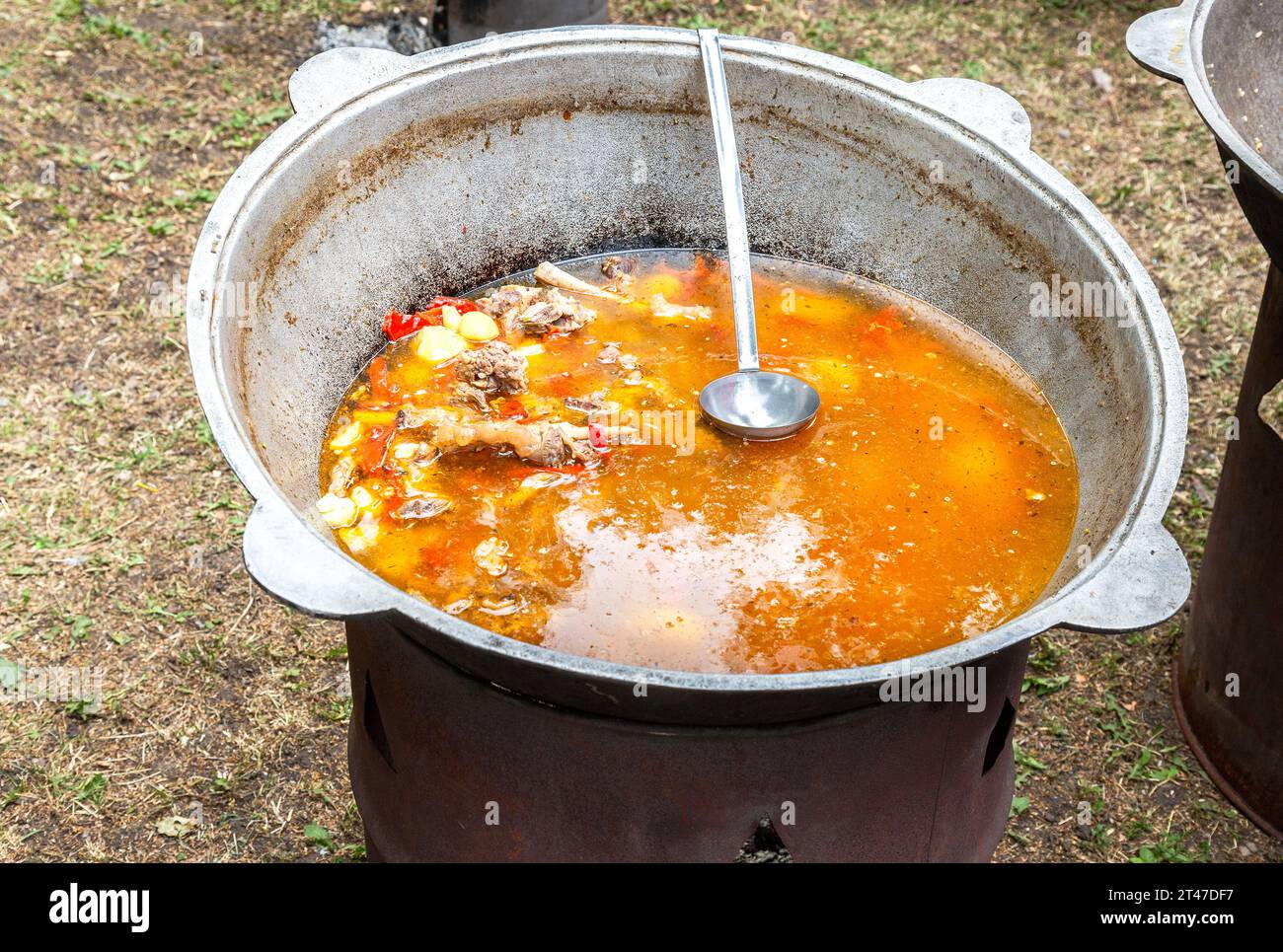 Kochen in einem großen Kessel orientalische Gerichte - Suppe. Suppe mit großem Gemüse und Fleisch. Shurpa in einem großen Kessel. Leckeres Street Food. Fleischsuppe Stockfoto