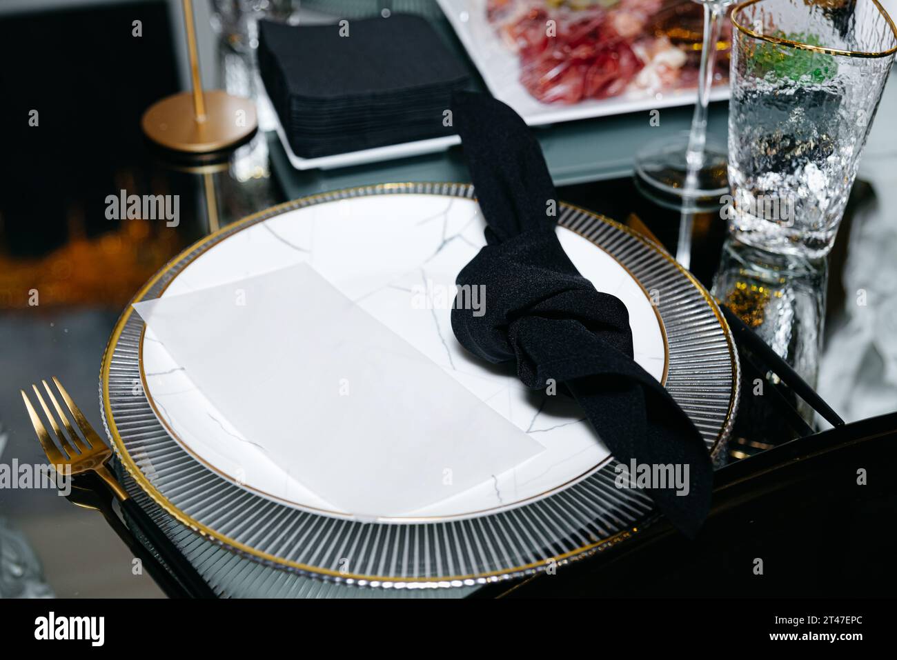 Eine schwarze Serviette, elegant geknotet und auf einem raffinierten Teller platziert, ziert einen Spiegeltisch im luxuriösen Ambiente eines Restaurants. Stockfoto